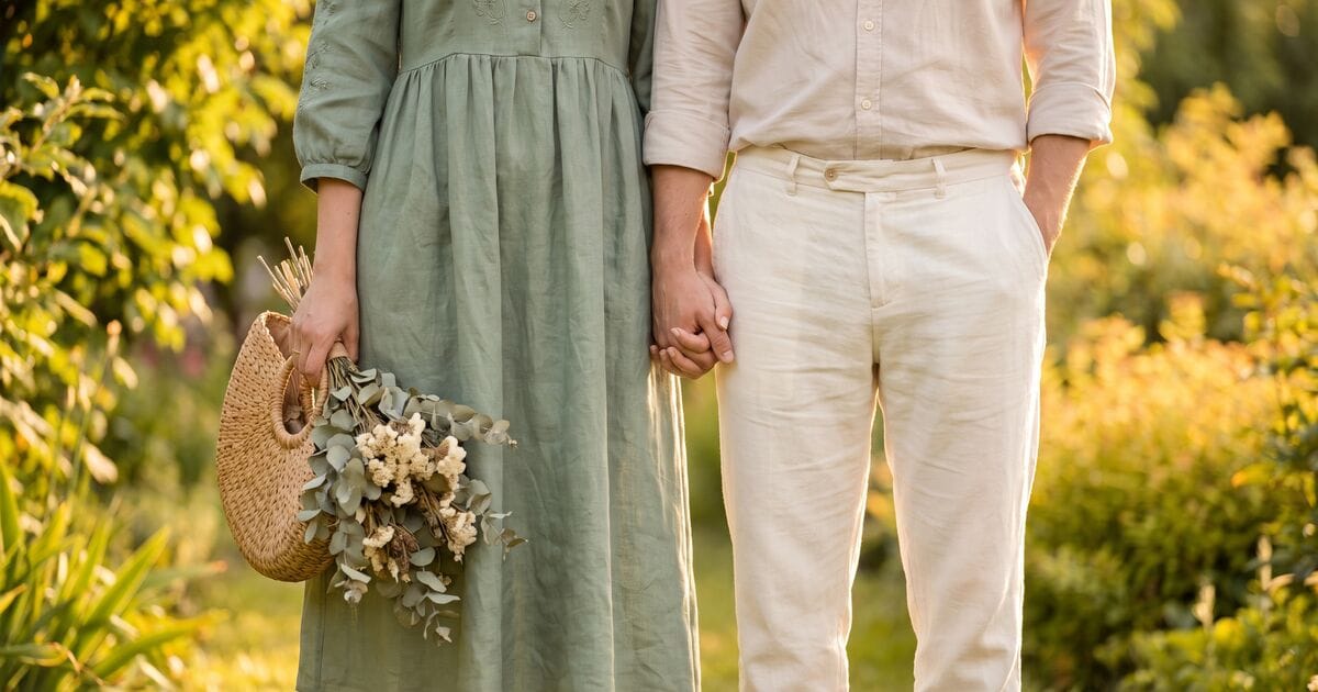 A couple in coordinated prenup outfits standing in a garden at golden hour, sage green dress and cream linen pants